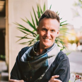 Theo Edmonds wearing a button-down shirt, blue jeans, and a loose scarf.
