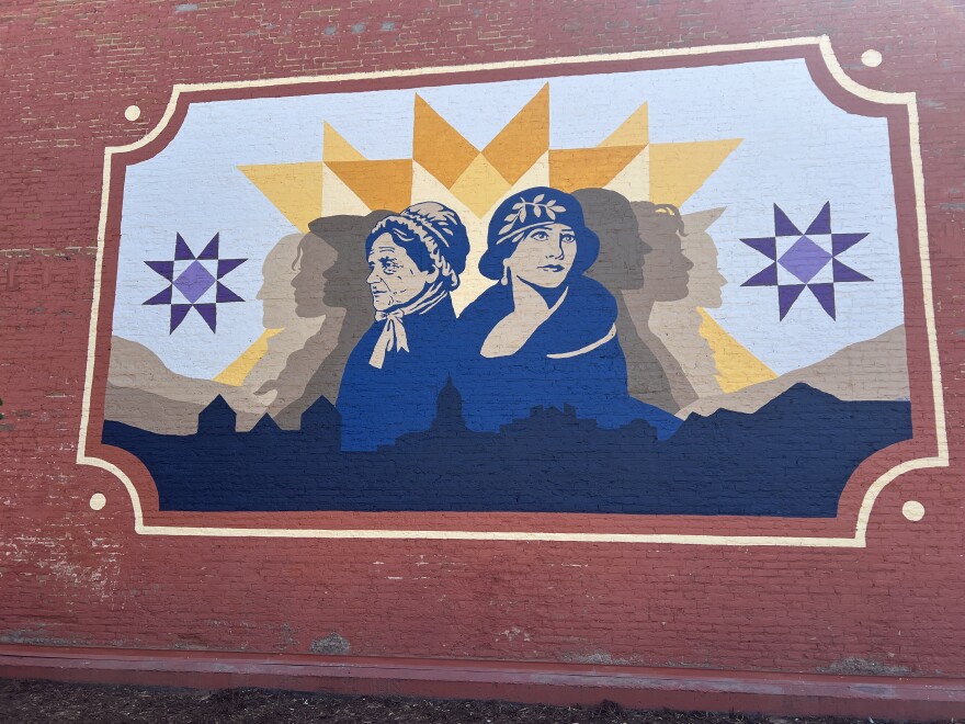 A mural of two women painted in blue on a red brick wall.