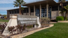 The entrance of the Washington County Administrative Building is framed between two palm trees. A large sign sits out front. 