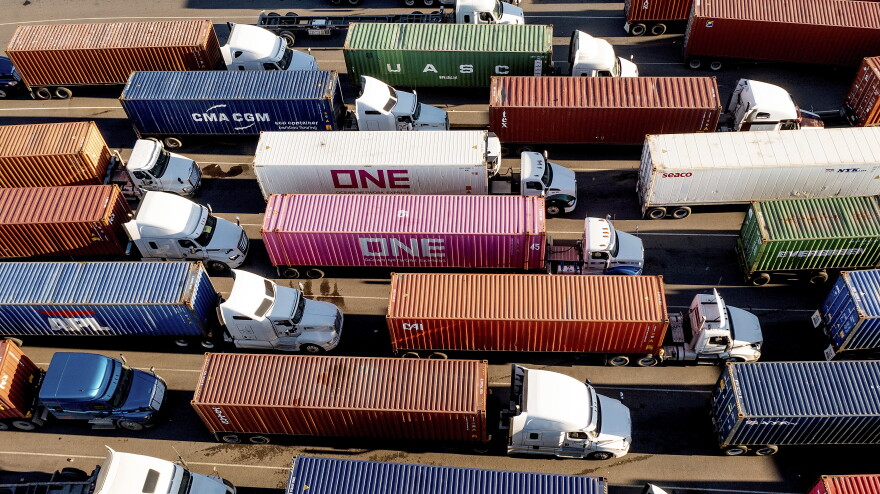Semi trucks carrying colorful shipping containers sit on a roadway.