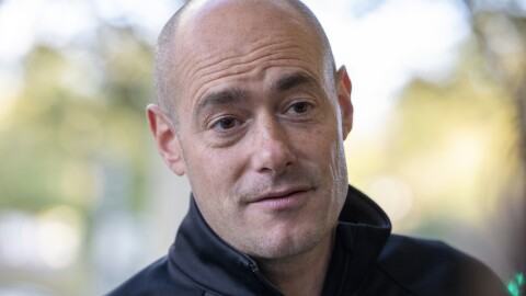 a close-up of a bald man in a black half zip sweater