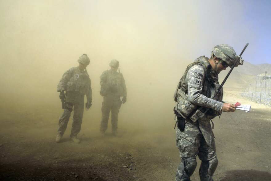 U.S. Army Staff Sgt. Brad Hollingsead, left, Lt. Rick Chersicla, center, and Capt. Brian Moran, all of 4th Battalion, 25th Field Artillery Regiment from Fort Drum, N.Y., brace themselves as a helicopter lands at their combat outpost in the Jalrez Valley in Afghanistan's Wardak Province on Friday, Sept. 25, 2009.