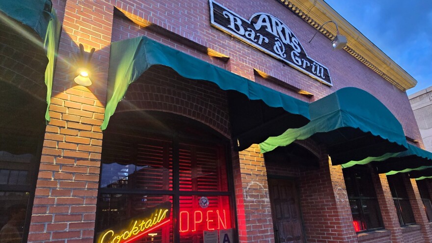 A reddish-brown brick building with the signs, “Arts Bar & Grill,” “Cocktails,” and “Open.”