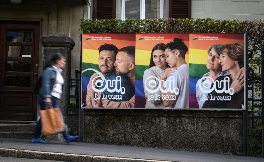 A person walks by a bus station advertisement with three same-sex couples against a rainbow background and the words "Oui, je le veux" or "Yes, I want it."