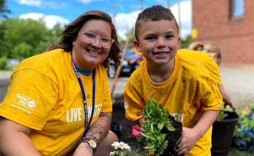 A woman and a boy in yellow t-shirts pose with flowers they are planting.