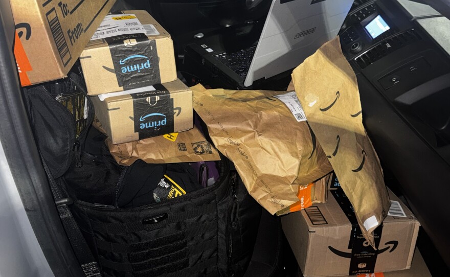 Stacks of Amazon boxes and paper parcels fill the passenger seat and floorboard of a police patrol car.