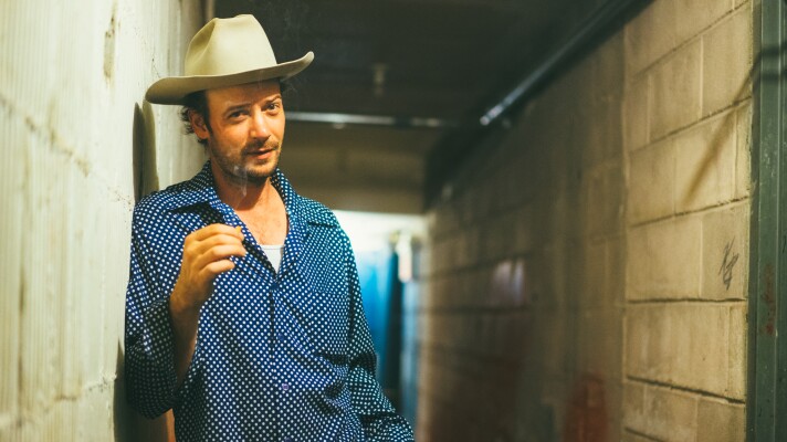 A man in a blue shirt and a white cowboy hat stands in a narrow hallway