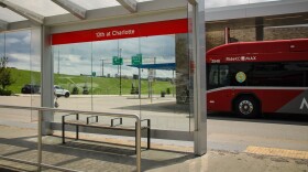 A bench with handrails in the middle sits at a bus shelter. Behind it is a red bus