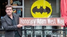 Actor who worked with Adam West holding a sign reading Honorary Adam West Way.