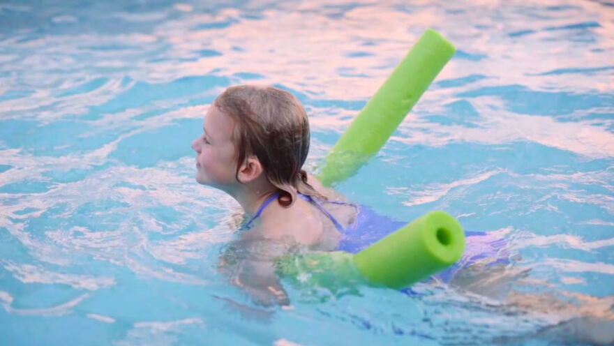 A little girl uses a swimming noodle to float in a scene from the FWDPC's YouTube video. 