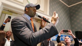 African American man in hat and suit talks into microphone with crowd 