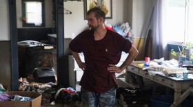 a man stands smoking a cigarette with his hands on his hips surrounded by debris