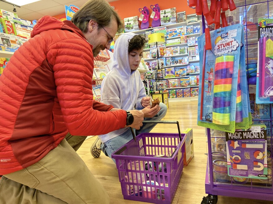 Oliver Yochem, 15, center, shows his father, Jonathan, the toys that he plans to buy at Learning Express Toys in Reno, Nev., on Friday, Dec. 16, 2022. 