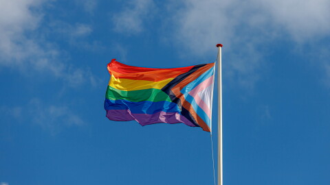 A Pride flag flies in a blue sky.