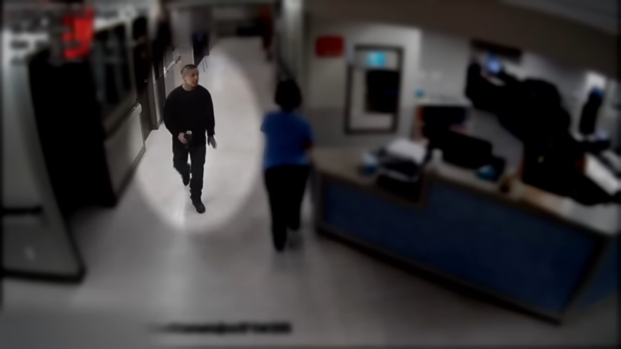 A man walks through a hospital hallway with a can in his hand. The rest of the image is slightly darkened and blurred except for a circular patch highlighting the man.