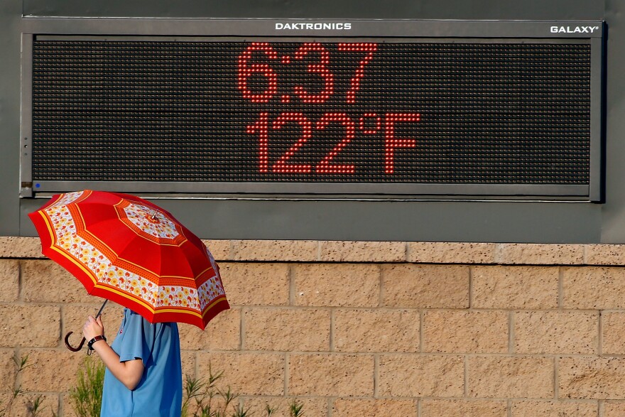 A pedestrian uses an umbrella to get some relief from the sun as they walk past a sign displaying the temperature on June 20, 2017 in Phoenix, Arizona.