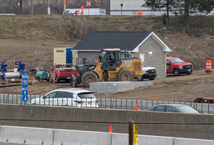 Construction equipment surrounds a small, cinderblock building.