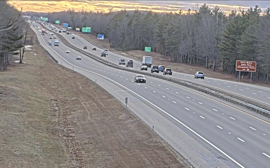 Long view of Maine Turnpike close to dusk with cars going both ways and signs alongside