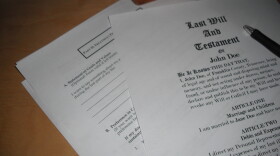 A series of papers on a wooden table. The first is titled "Last Will and Testament of John Doe" followed by legal text.