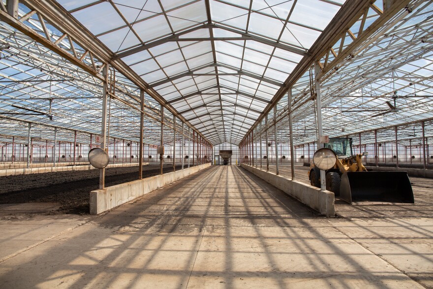 What looks like a large, glass-paneled greenhouse, except the class is uncolored and clear. The sludge at this distant just looks like dirt spread across the floor. To the right is a yellow and black front loader construction vehicle.
