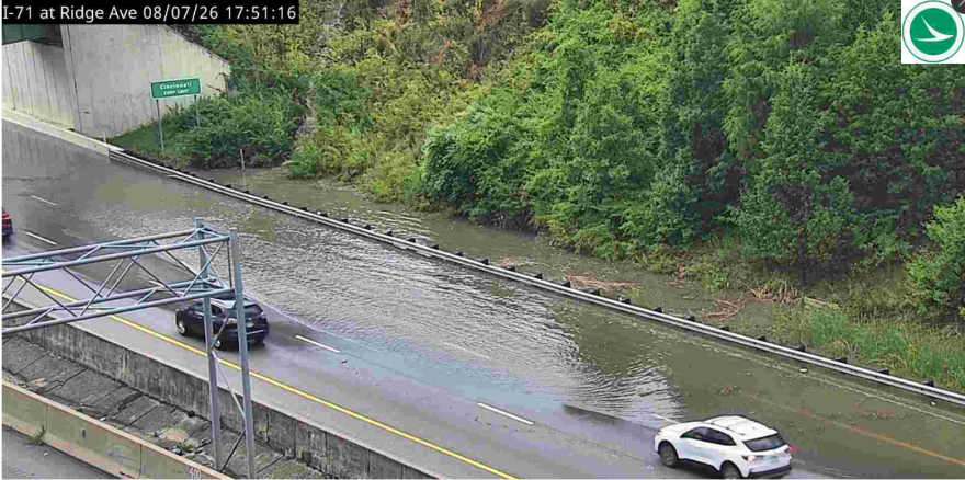 Floodwaters cover lanes of a highway as cars pass.
