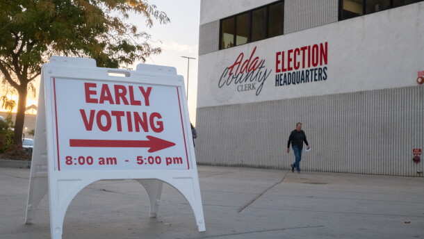 A man walks in front of a beige building near a sign indicating early voting is underway.