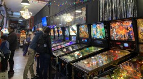 Pinball machines lined up under decorative string lights at Free Gold Watch. 