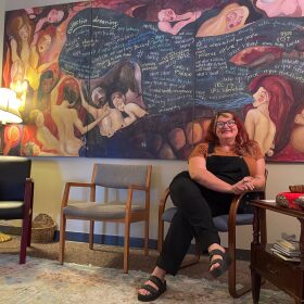 Christine Wilson, executive director of Women Writing for (a) Change sits underneath a painting donated by a former student of the program.