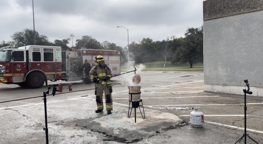 Un bombero pone un pavo en una cazuela con aceite para una demostración de seguridad. Detrás de él hay un camión de bomberos. 