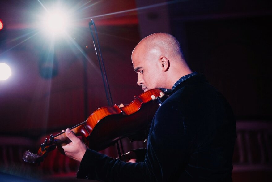 A person with a brown violin in a blue coat with a white light shining 