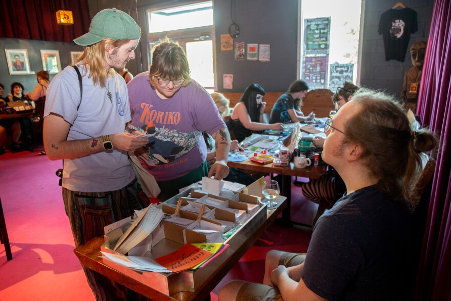 Two people look through Nick's table, whivch hosts several of his one-page zines, selling from between .25 a piece to $2.