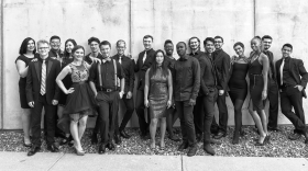 A black-and-white group photo, apparently outside against a concrete background, of young men and women in formal wear. 