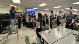 Kevin Spencer stands on a chair with his left arm outstretched to explain a magic trick to a classroom of students at the University of Alabama at Birmingham. The students stand mimicking Spencers position.