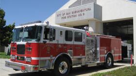 A large fire truck sits outside a fire station. A sign on the station reads 'City of San Buenaventura Fire Station No. 6.'
