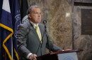 A man in a grey suit with a gold tie stands behind a podium.