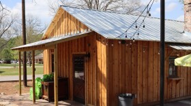 A small wooden building with a metal roof and string lights is shown outdoors.
