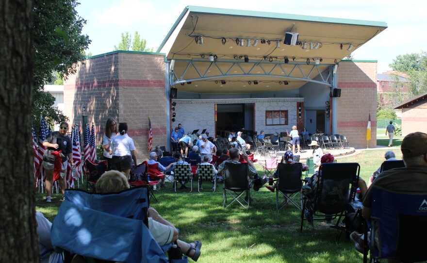 Eventgoers in lawn chairs sit near the amphitheater stage as members of the Bloomington-Normal Community Concert Band set up their music stands and instruments.