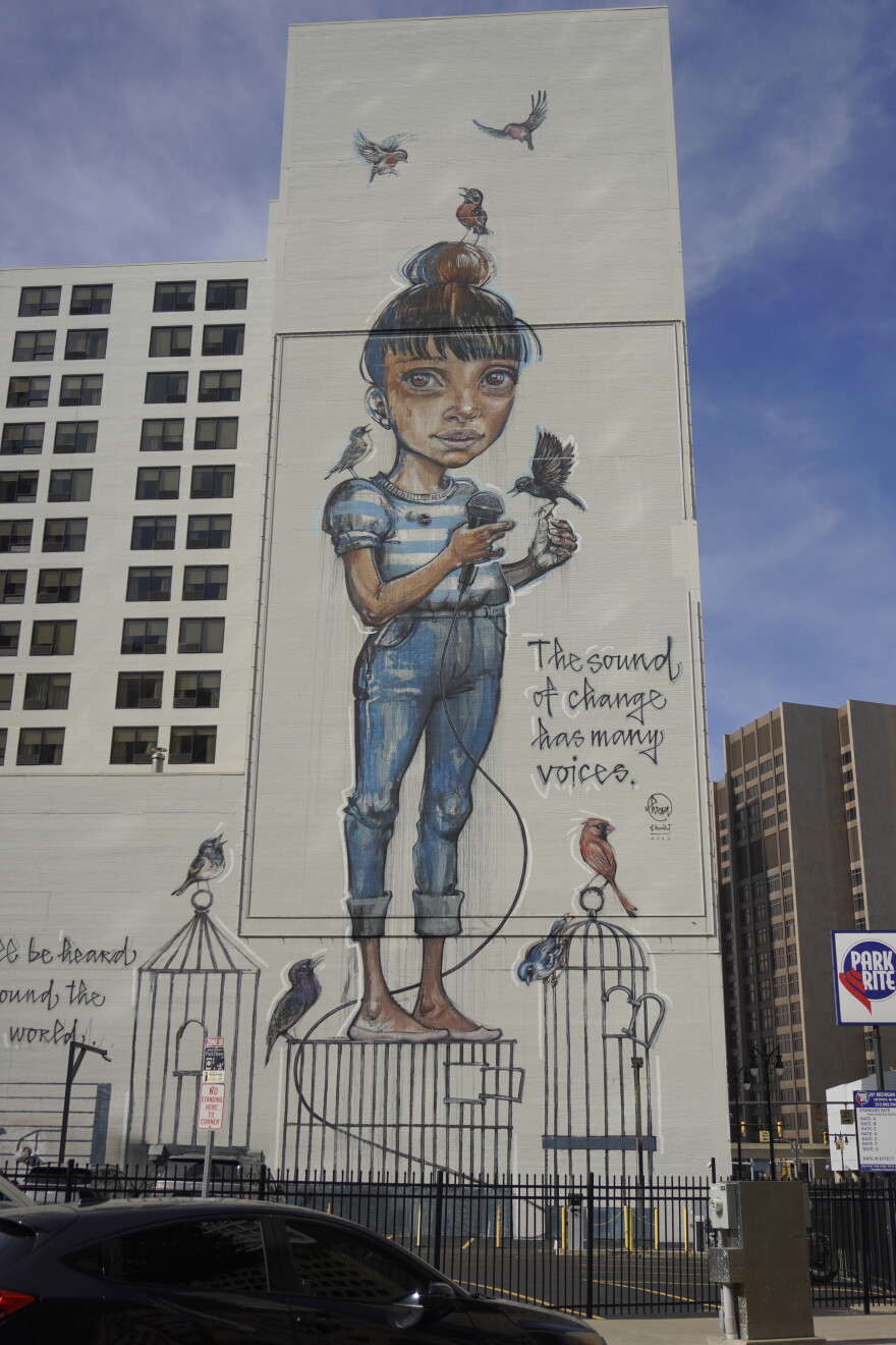 A multistory mural shows a girl holding a microphone, surrounded by birds and birdcages.