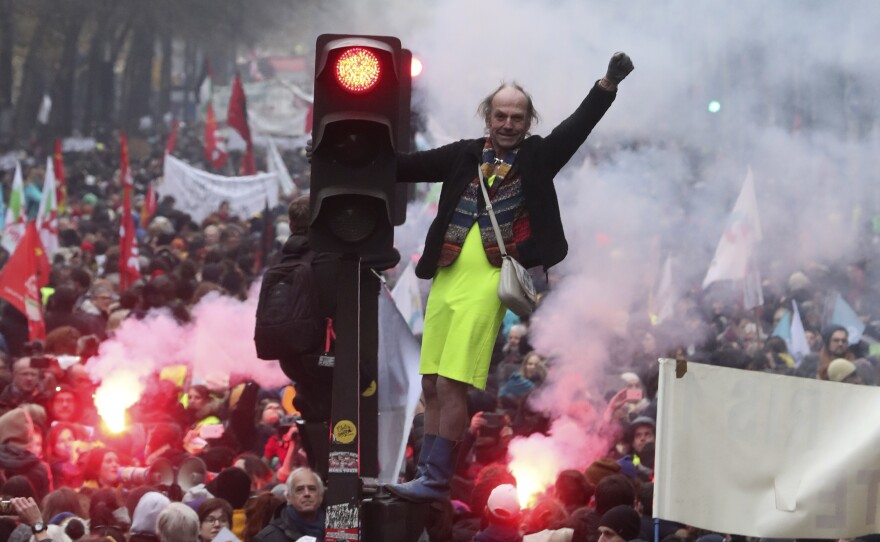 A man perched on a traffic light pumps his fist amid the chaos of a demonstration Thursday in Paris. Several thousand protesters took part in open-ended nationwide strikes, begun Thursday under union leadership.