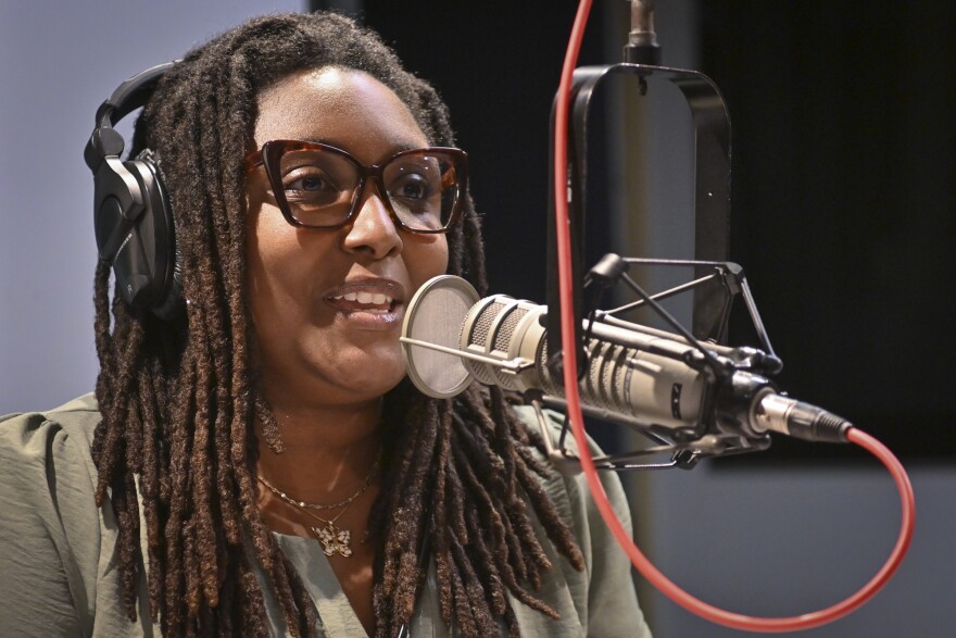 A person sits inside a radio studio talking at a microphone.