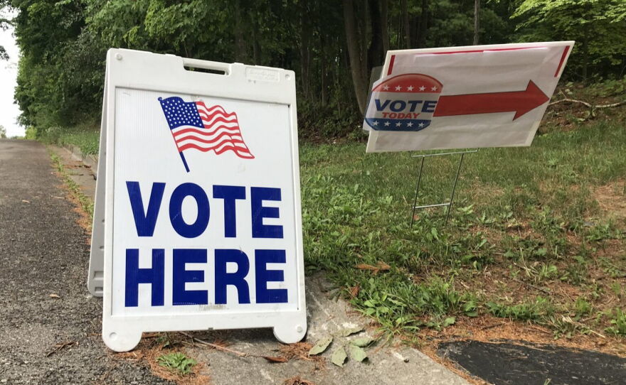 A sandwich board sign with blue lettering and an american flag advertises where to vote.