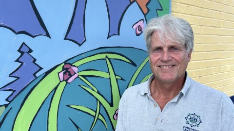 A man wearing a grey polo standing in front of a mural of leaves and forest creatures