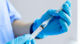 A health practictioner, mostly off-camera, fills a syringe with clear liquid.