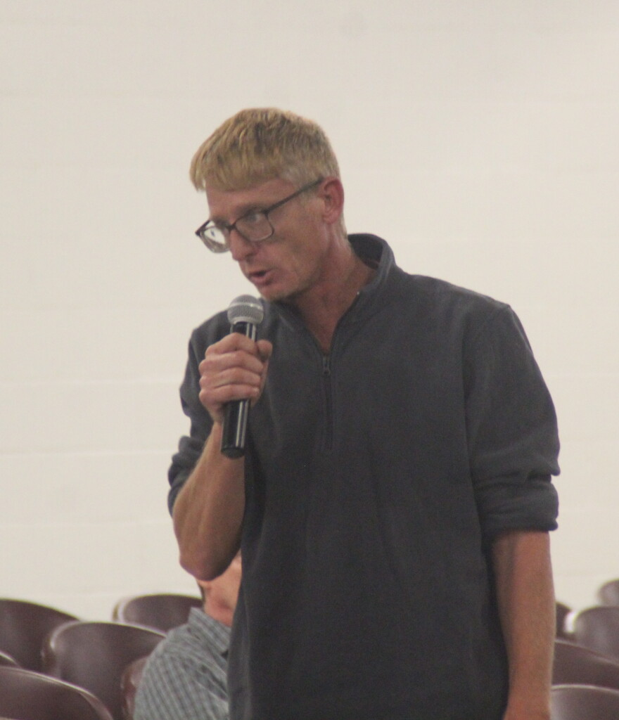 A man speaks into a microphone while providing public comment. 