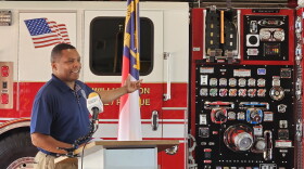 A man gestures to a fire truck while standing at a lecturn.