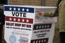 A voter drops off their ballot at a ballot drop box outside that has red white and blue coloring.