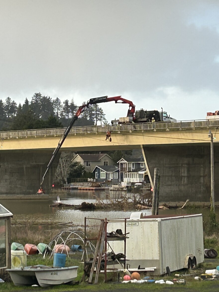 A hydraulic arm reaches from atop a bridge into the water below