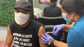 Calvin Gough, a 54-year-old from Washington, D.C., gets his first dose of the Pfizer vaccine while sitting in a barber chair. (Dominique Maria Bonessi/WAMU)