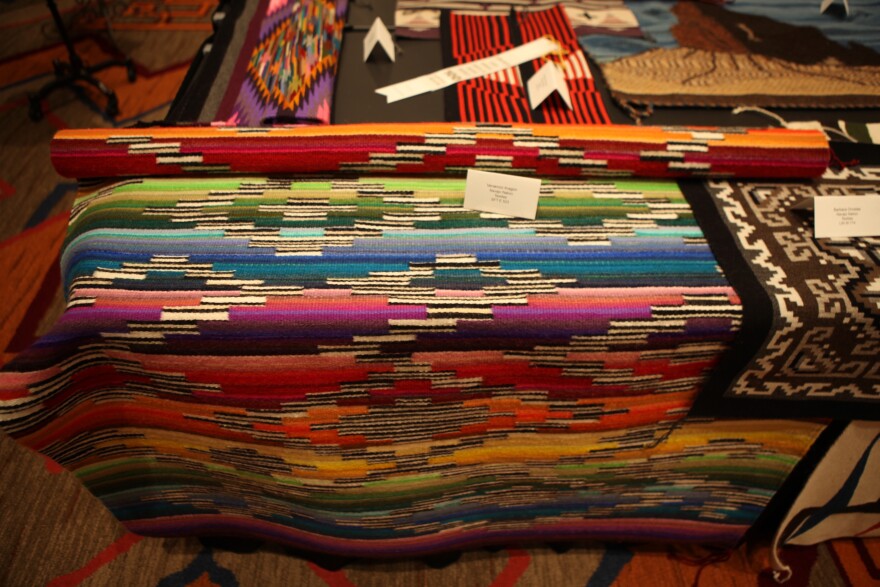 A woven textile on display, with rainbow color stripes punctuated with monochrome forms