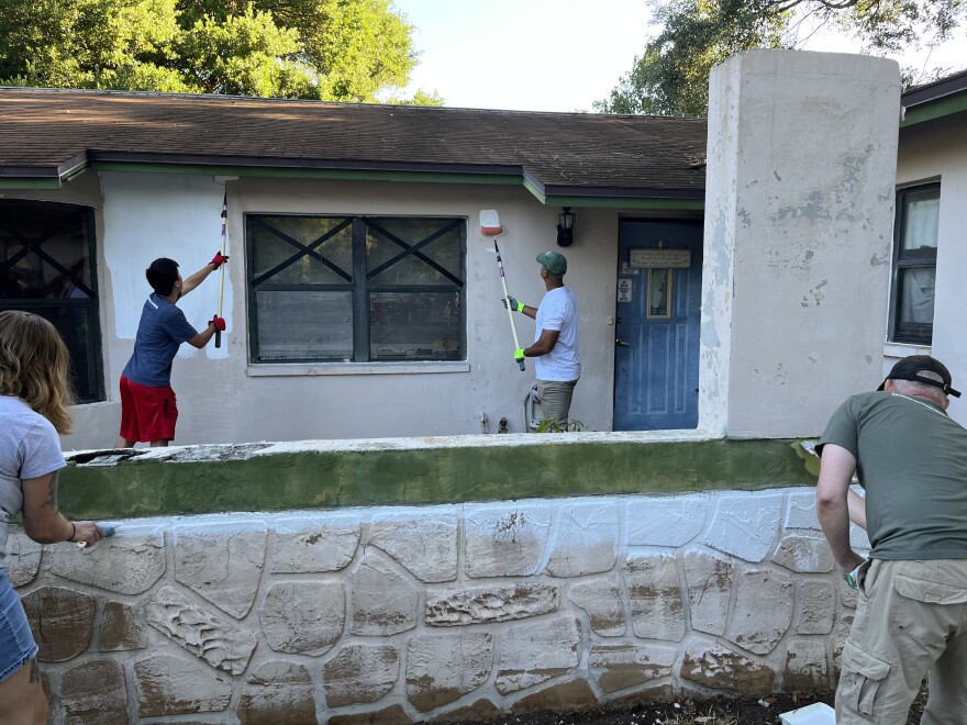 Three men and one woman paint a house with white paint.